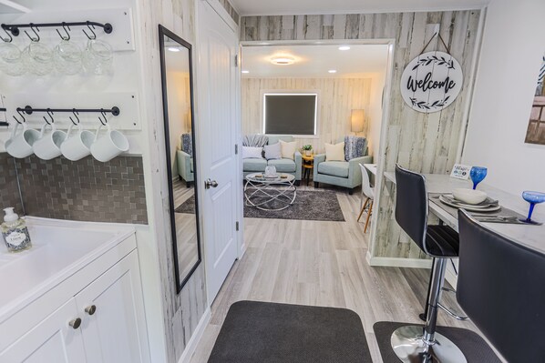 A modern kitchen with hanging glassware, a dining area with a 'Welcome' sign, and a cozy seating area with a view of the city. - Adorable cottage with king Size bed and a short distance to WW University (Walla Walla)