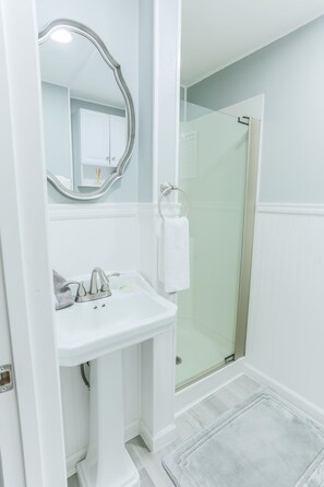 A bathroom with a pedestal sink, a mirror, a towel rack, and a glass shower enclosure. - Adorable cottage with king Size bed and a short distance to WW University (Walla Walla)