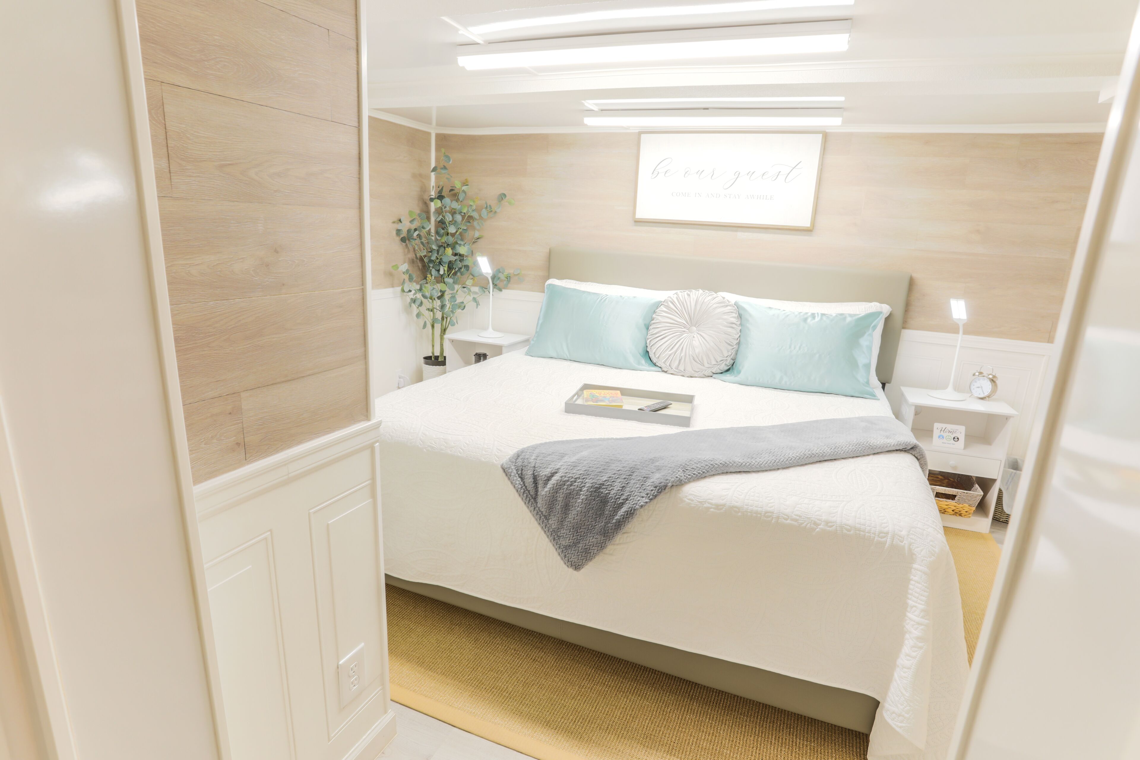 A neatly arranged bedroom with a bed, bedside tables, a nightstand, a wall-mounted light, and a framed quote.