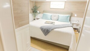 Une chambre à coucher bien rangée, avec un lit, des tables de chevet, une petite table, une lampe fixée au mur et un cadre contenant une citation.
