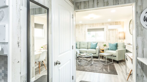 Un salon moderne avec un canapé, une table basse et un coin repas visible à travers une porte ouverte.