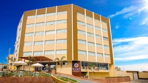 Ein mehrstöckiges Hotel mit beige farbenem Mauerwerk, großen Fenstern und einem Schild, das es als KIMO Palace Hotel in Fortaleza kennzeichnet.