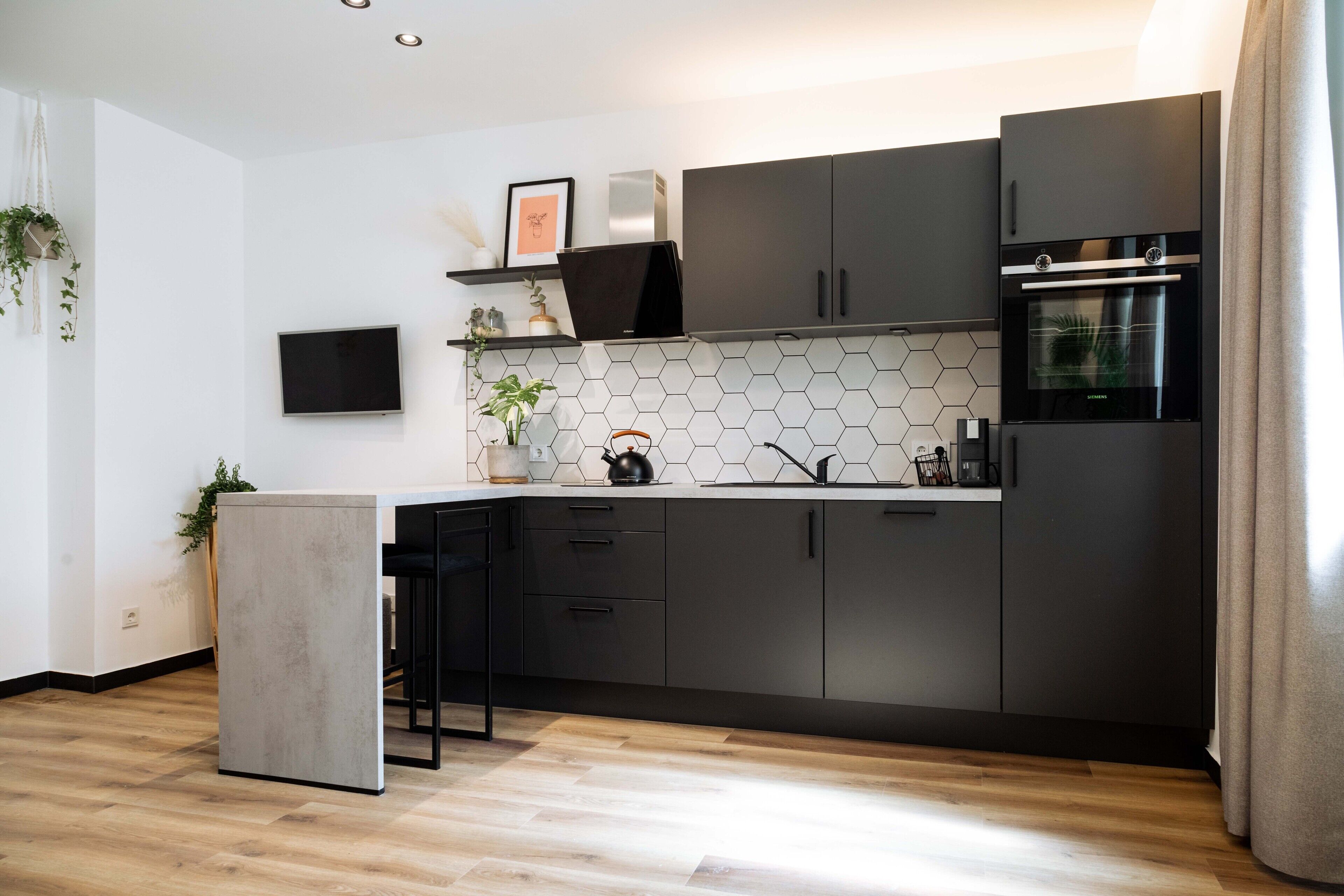 A modern kitchen with dark cabinets, a built-in oven, and a hexagonal tile backsplash.