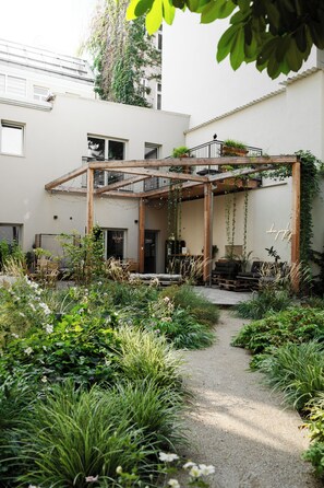 Zona exterior coberta amb una pèrgola de fusta, seients i vegetació abundant.