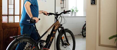 A man in blue attire adjusting a mountain bike in a room with a checkered floor, wooden door, and a light fixture.