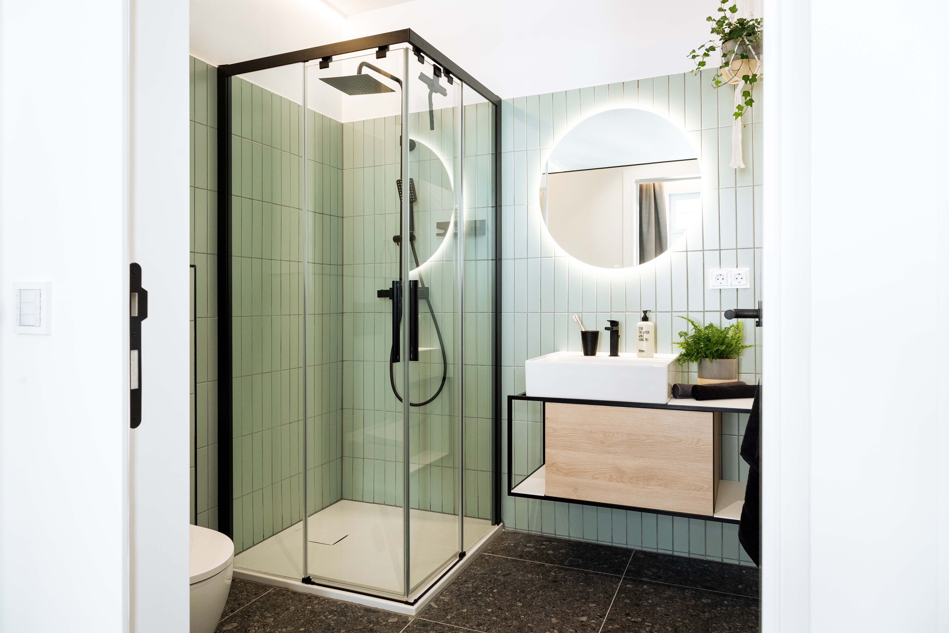 Un baño moderno con cabina de ducha de vidrio, un lavamanos blanco y un espejo con marco circular.