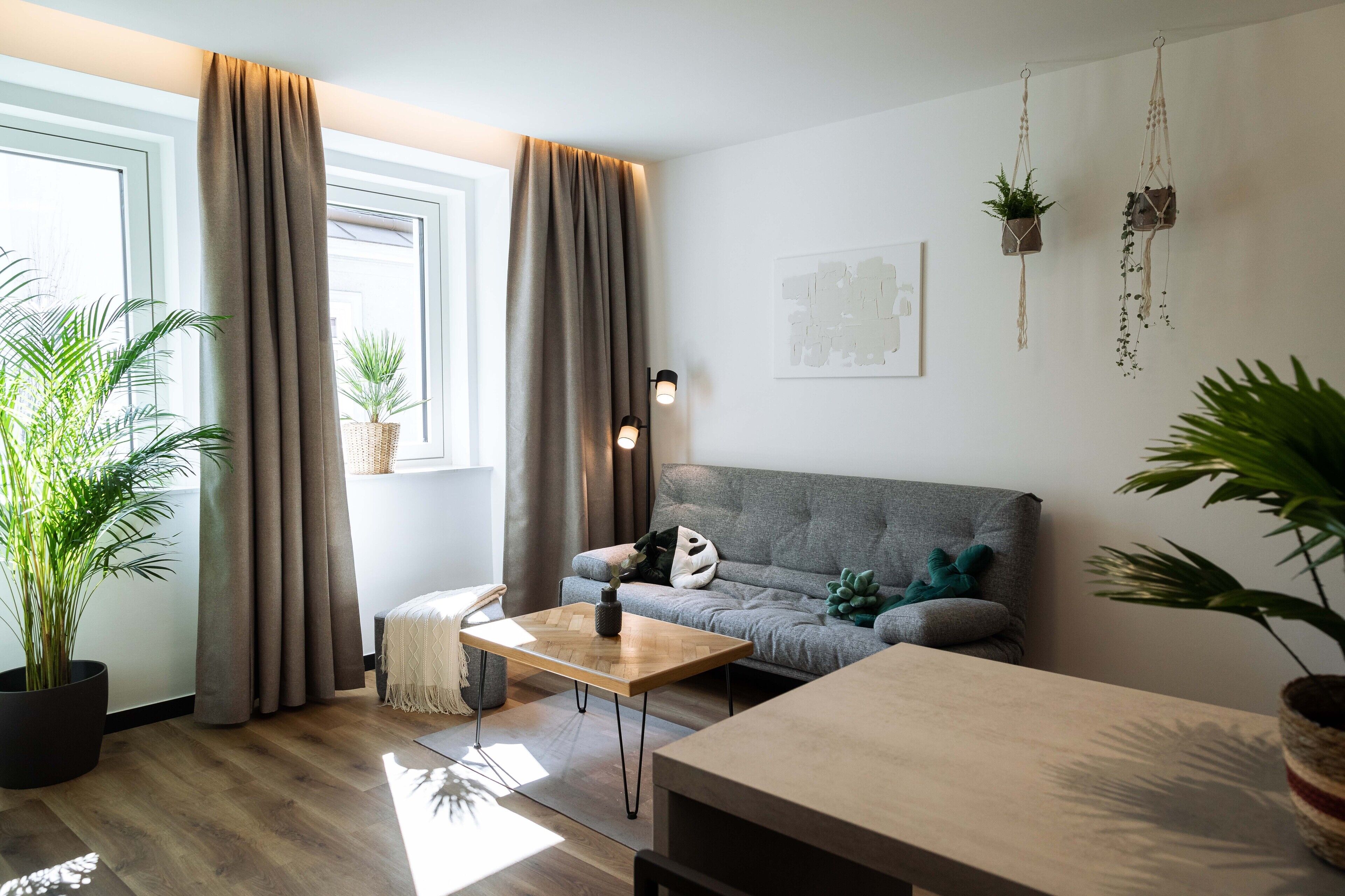 A modern living room with a grey sofa, a wooden coffee table, and a large potted plant.