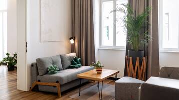 Een moderne woonkamer met een grijze bank, een houten salontafel en een kamerplant.