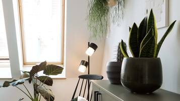 Una sala de estar moderna con piso de madera, un sillón mecededor, un escritorio con lámpara y plantas en macetas.