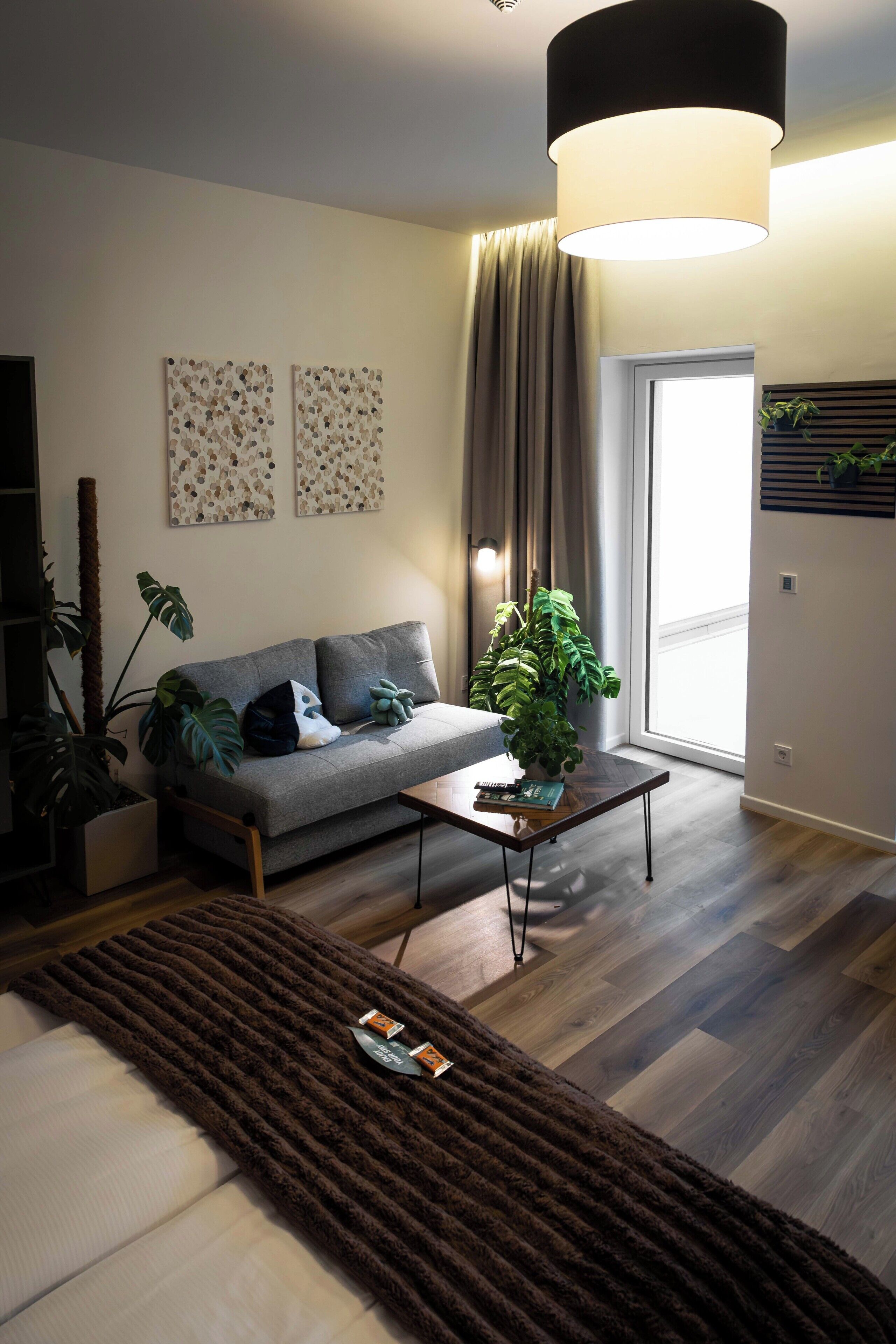 A modern living room with a grey sofa, a coffee table, and a large window.