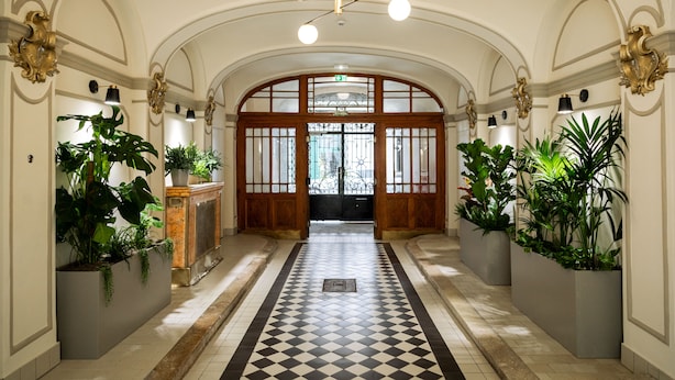 Een hal met een zwart-wit geruit vloerkleed, een gewelfde plafond en potplanten.
