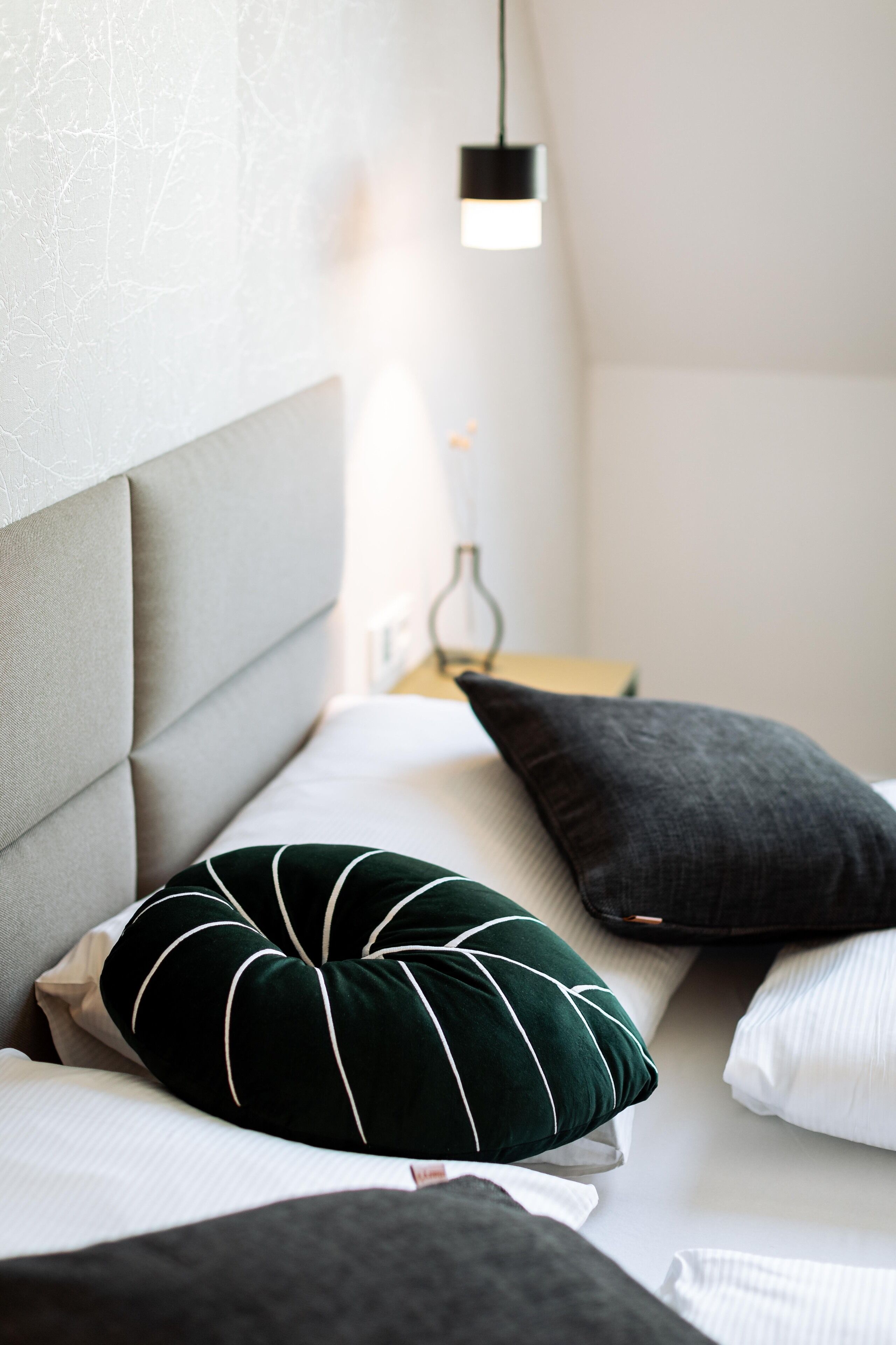 A neatly made bed with a grey headboard, a green striped pillow, and a dark grey pillow.