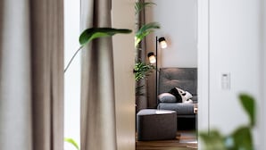 Een moderne woonkamer met een bank, een salontafel en een lamp. Voorop staat een plant en een gordijn.