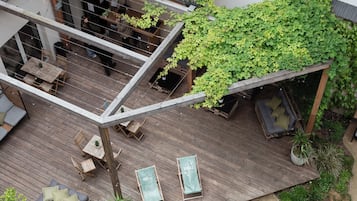 A rooftop terrace with wooden flooring, seating areas, and a variety of plants.