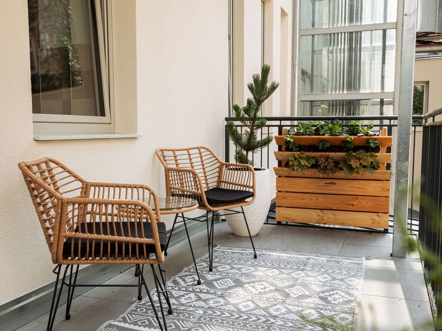 Un balcón con sillones de mimbre, una planta en maceta y un jardín vertical con follaje.