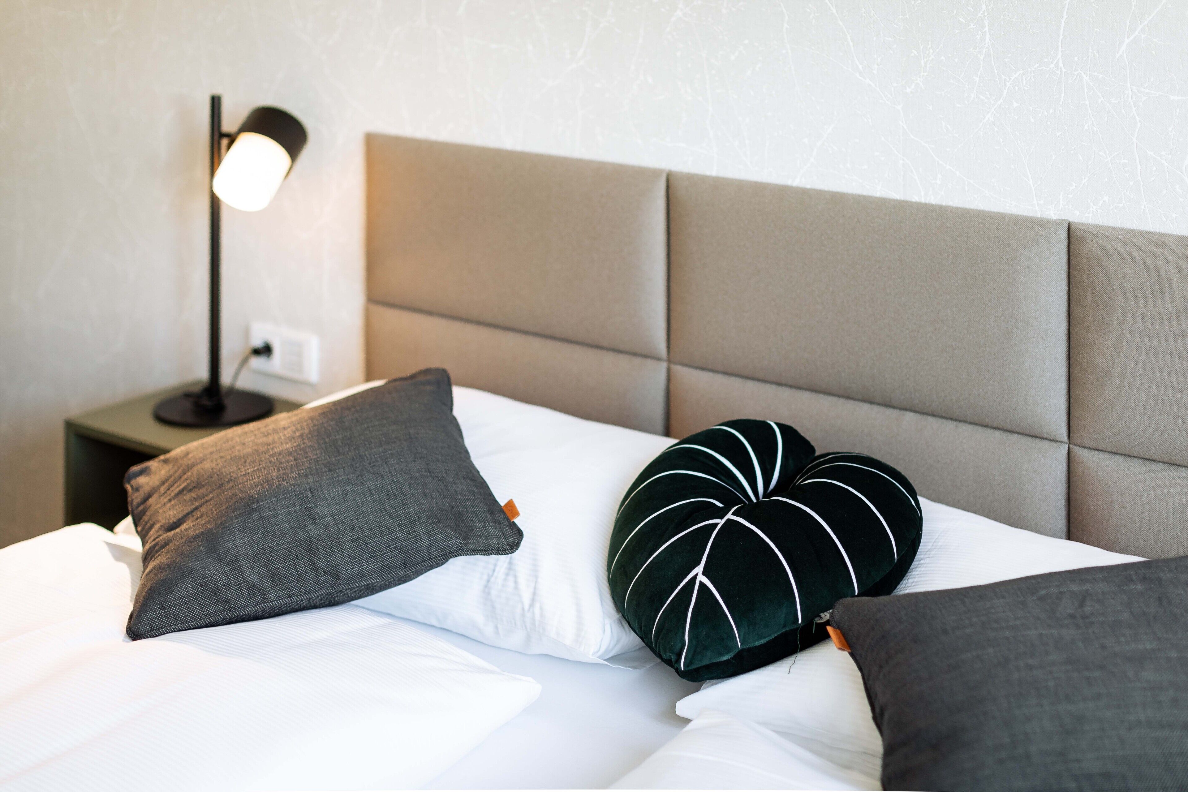 Ein ordentlich bezogenes Bett mit weißen Leinentüchern und mehreren Kissen, darunter eines in Herzform.