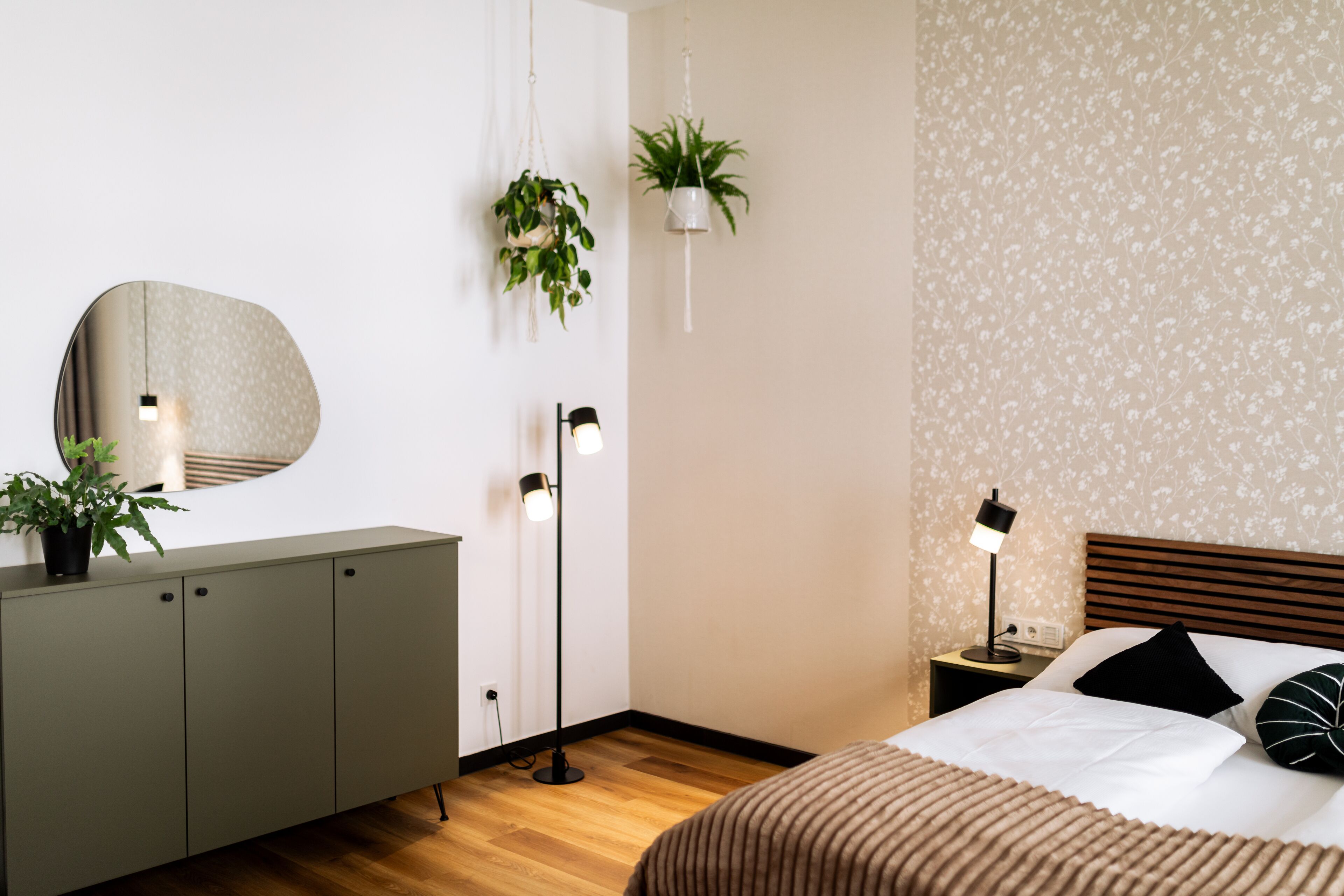 Un dormitorio con cama, mesita de noche, lámpara y un espejo sobre un mueble.