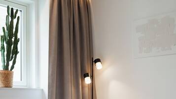 A bedroom with a bed, a nightstand, a window with a cactus, and a wall-mounted lamp.