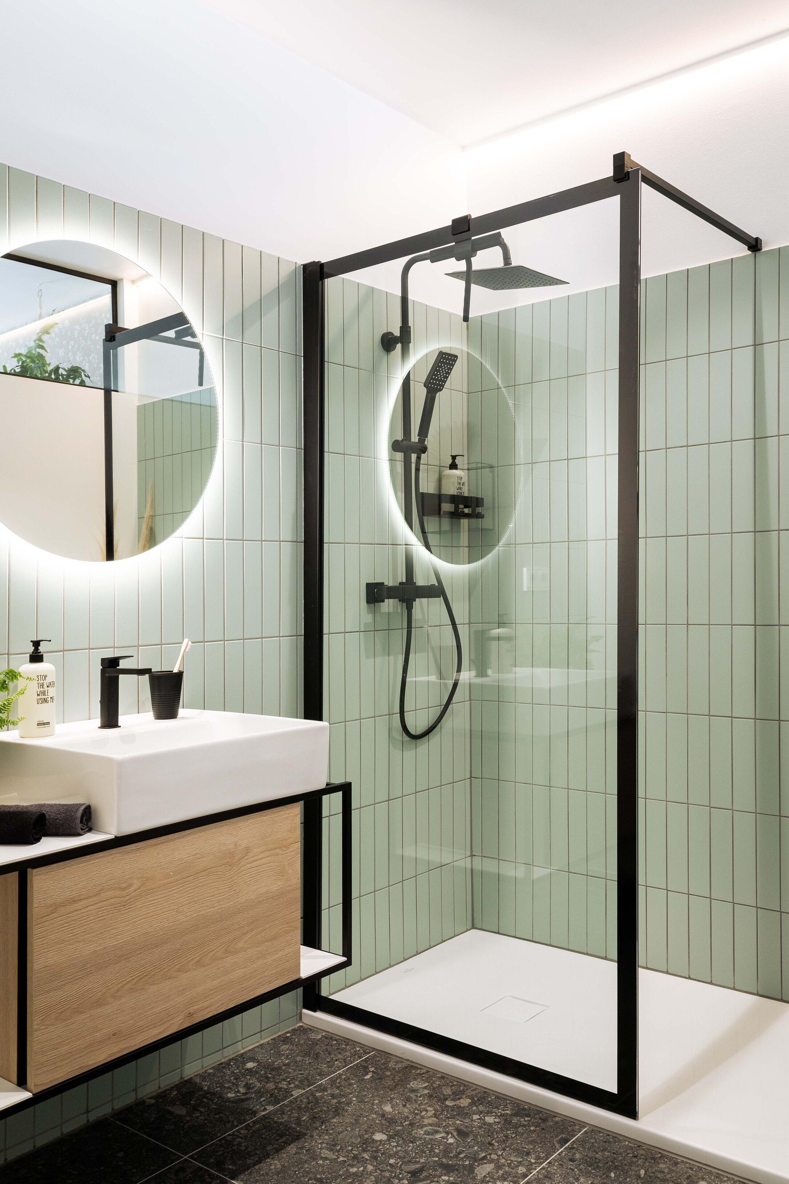 Une salle de bain moderne avec une douche à parois de verre, un lavabo blanc avec un meuble en bois et un miroir rond.