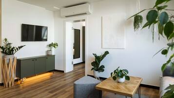 Ein modernes Wohnzimmer mit einem Flachbildfernseher, einem grünen Schrank, einem Holztisch und verschiedenen Topfpflanzen.