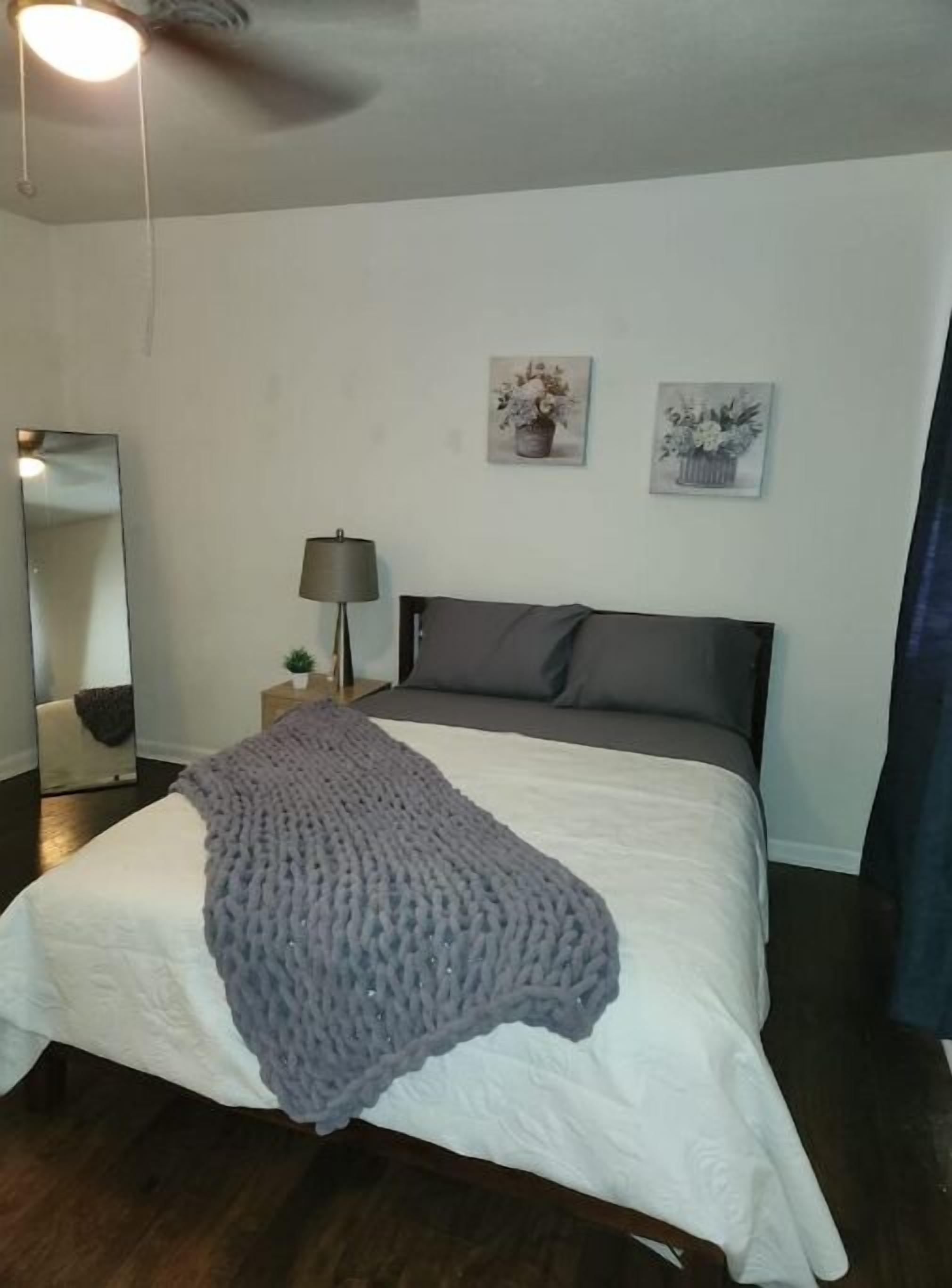 A bedroom with a bed, a bedside lamp, a mirror, and two wall-mounted pictures.
