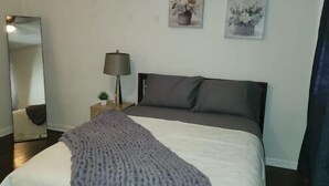 Un dormitori amb un llit, una làmpada de nit, un mirall i dues quadres penjats a la paret.