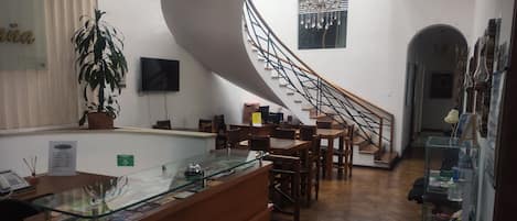 A reception area with a glass counter, wooden furniture, a staircase, and a potted plant.