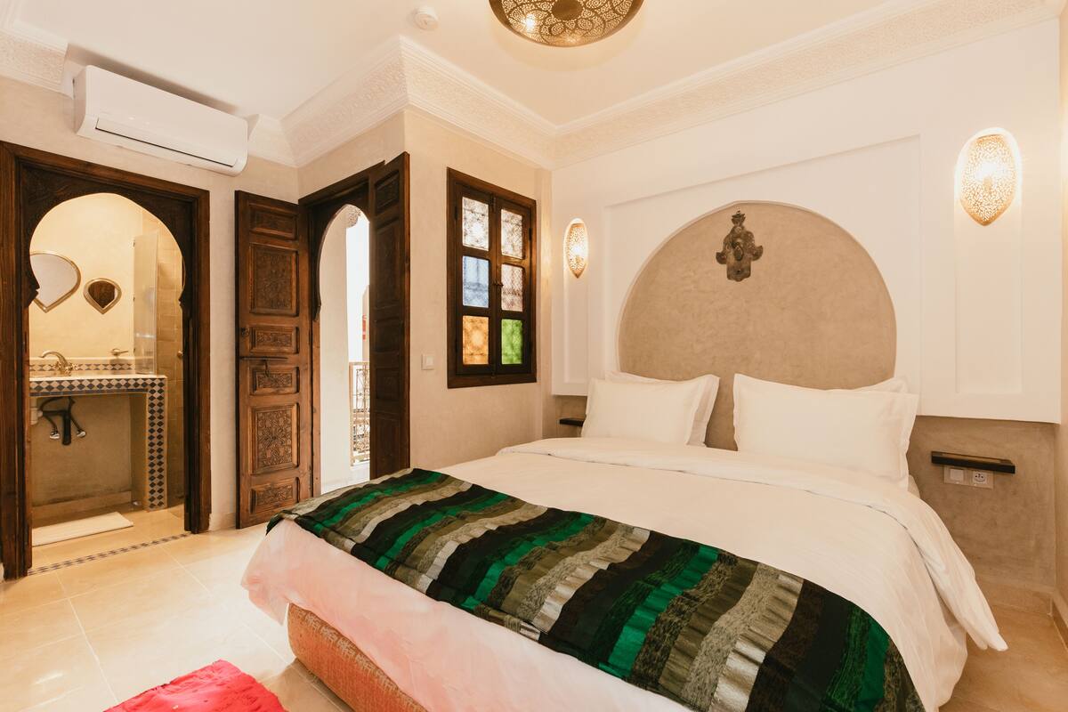 Un dormitorio con una cama grande, una puerta de madera, un espejo y una lámpara fijada a la pared.
