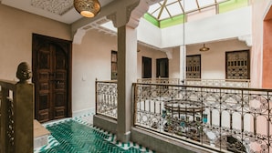 Um interior em vários níveis com chão de azulejos, grades decoradas e uma porta de madeira.