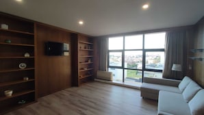 Un salon spacieux doté d’une grande fenêtre, d’étagères en bois, d’un canapé et d’un téléviseur à écran plat.