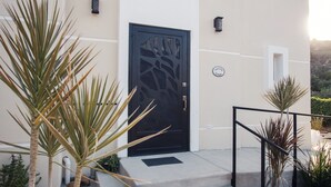 Un bâtiment avec une porte noire, un petit espace extérieur agrémenté de plantes et une enseigne sur le mur.