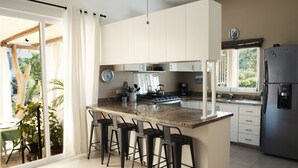 Une cuisine moderne dotée d’un grand îlot central, de tabourets de bar, d’un réfrigérateur et offrant une vue sur l’extérieur.