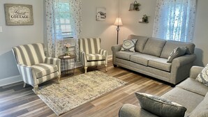 A living room with a striped armchair, a sofa, a round side table, and a floor lamp.
