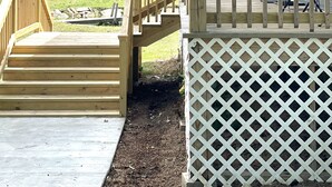 A wooden deck with a white lattice fence, a flag, and a view of a green landscape.
