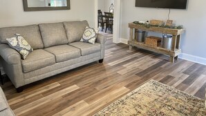 A living room with a grey sofa, a wooden coffee table, a flat-screen TV, and a patterned rug.