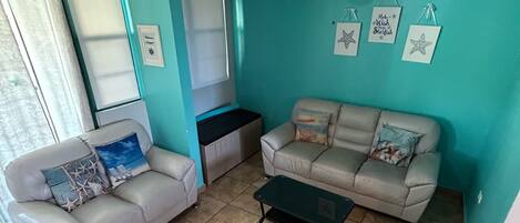 A living room with two sofas, a coffee table, a ceiling fan, and starfish decorations on the wall.