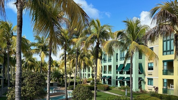 Un complexe hôtelier doté d’une piscine, de palmiers et d’un bâtiment agrémenté de nombreux balcons.
