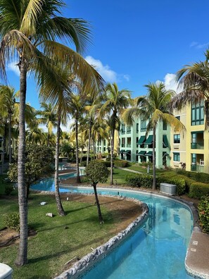 Un complexe hôtelier doté d’une piscine, de palmiers et d’un bâtiment agrémenté de nombreux balcons.