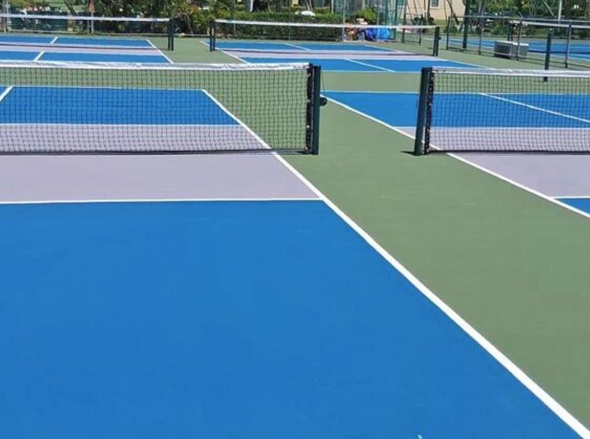 A tennis court with a net, green and blue playing surfaces, and surrounding fencing.