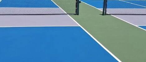 A tennis court with a net, green and blue playing surfaces, and surrounding fencing.