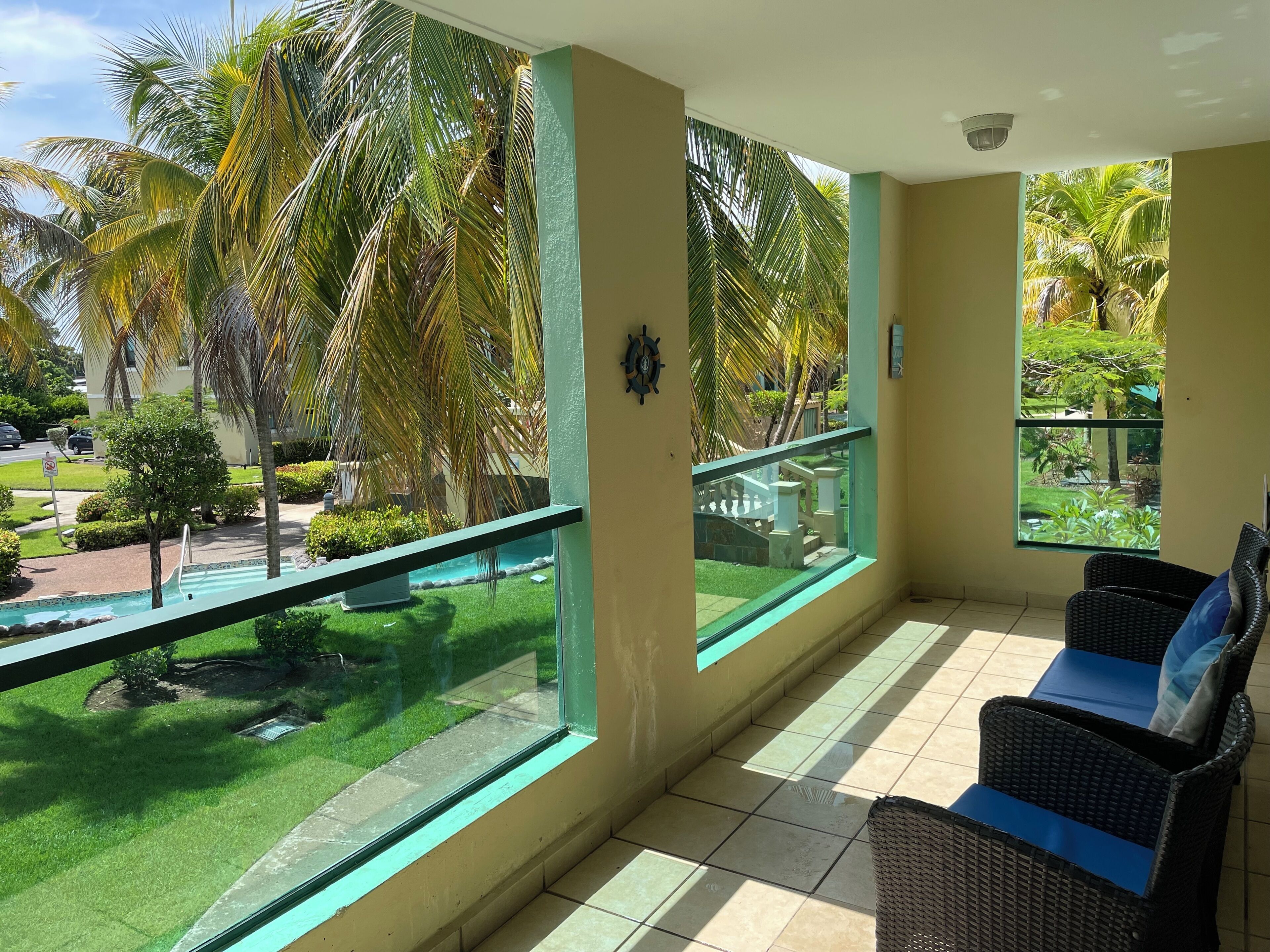 A balcony with a view of a swimming pool, palm trees, and a tiled floor.