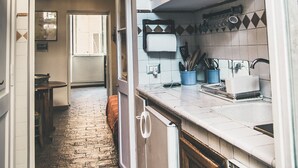 Une cuisine étroite avec un sol en briques, des placards blancs et un luminaire suspendu.