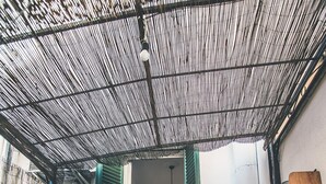 Un couloir étroit avec un plafond en bambou, des volets verts et un banc.