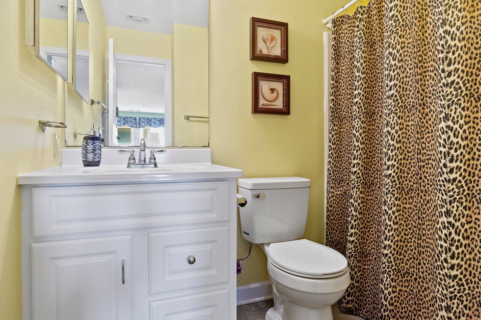 A bathroom with a white vanity, a toilet, and a leopard print shower curtain.