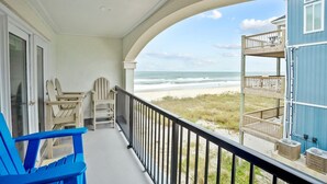 Ein Balkon mit Blick auf den Strand, zwei Adirondack-Stühle und ein blauer Stuhl.
