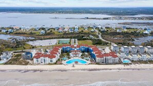 Luftaufnahme eines Küstenresorts mit mehreren Gebäuden, einem zentralen Schwimmbecken und direktem Strandzugang.