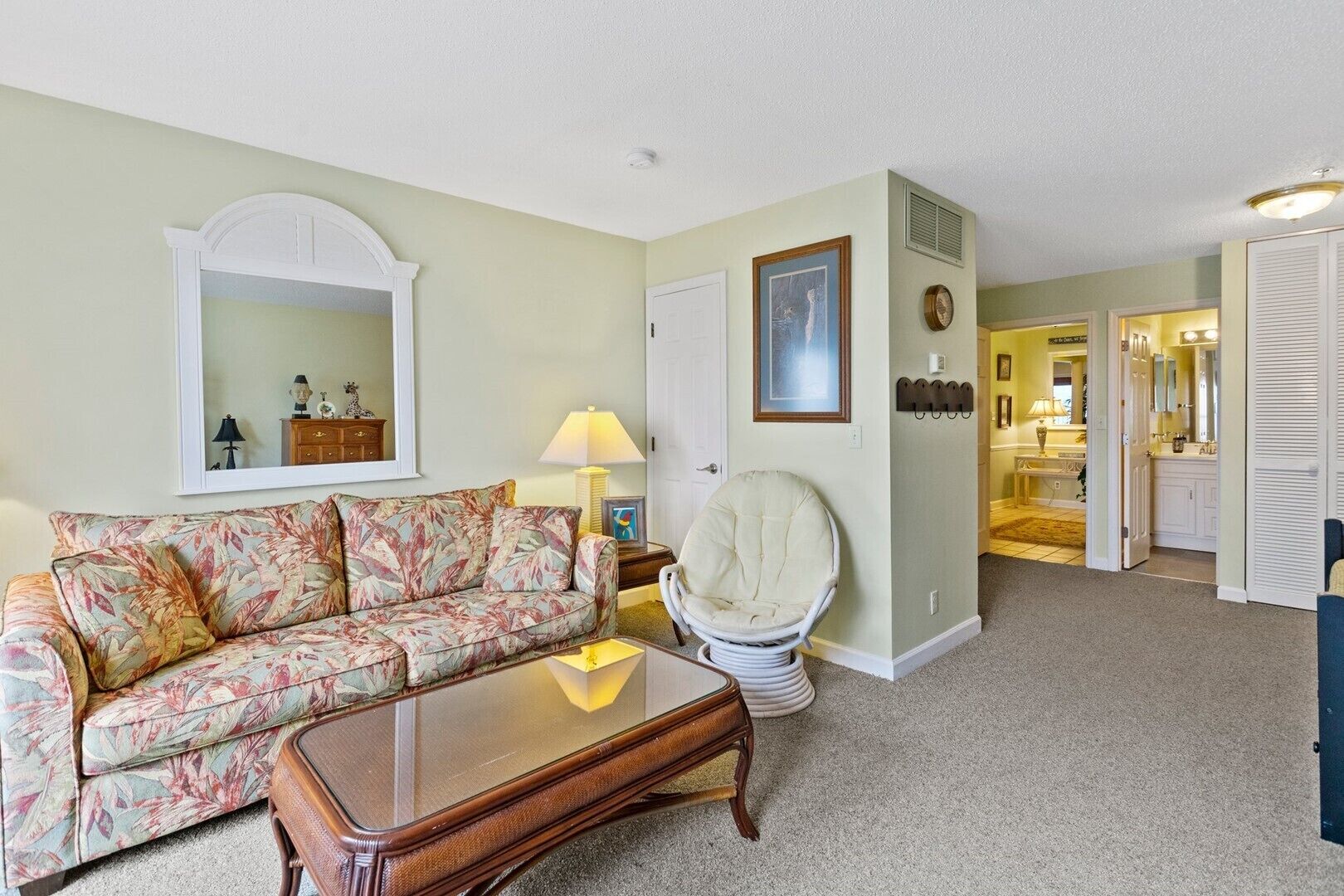 A living room with a floral sofa, a round chair, a wooden coffee table, and a mirror on the wall.