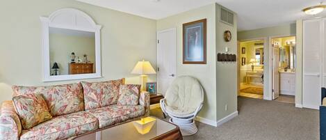 A living room with a floral sofa, a round chair, a wooden coffee table, and a mirror on the wall.