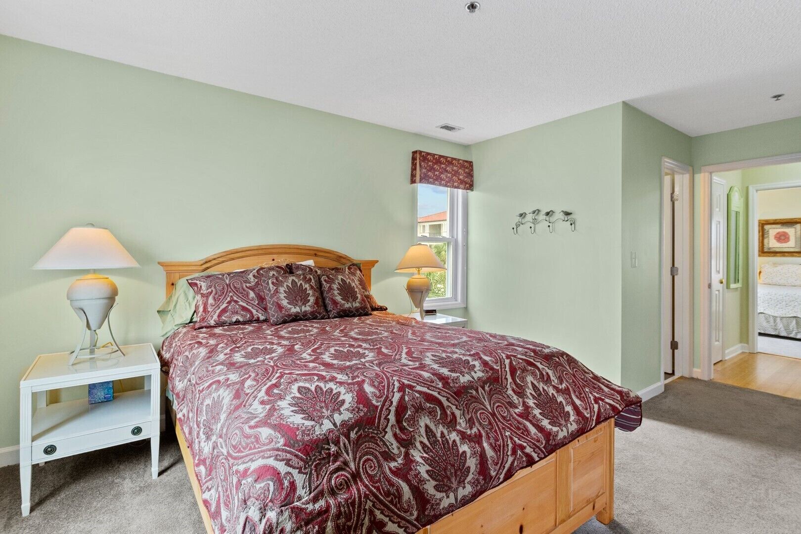A bedroom with a wooden bed, a nightstand with a lamp, a window with a view, and a door leading to another room.