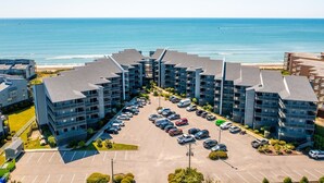 Ein mehrstöckiges Hotel mit Parkplatz davor, nahe einem Strand mit dem Meer im Hintergrund.